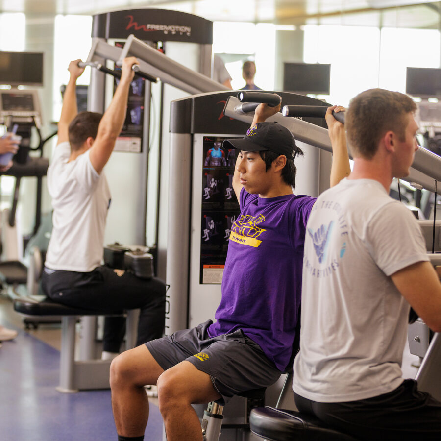 Three young adults pose in lat pull down machines at Perry Center