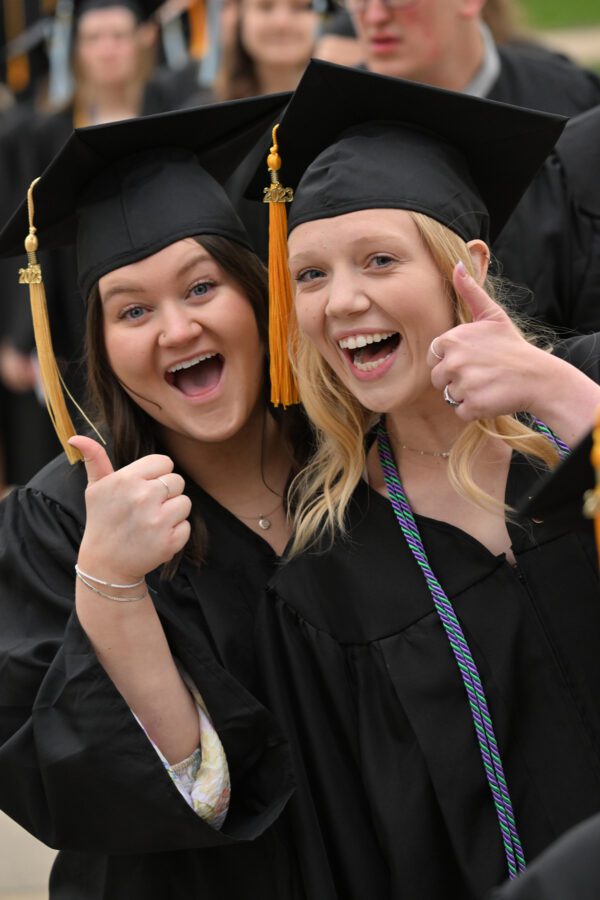 Two girls give a thumbs up wearing their cap and gowns