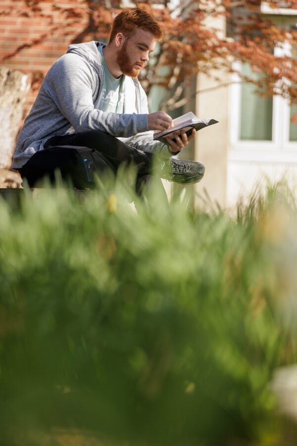 Photo of male student reading in the Quad