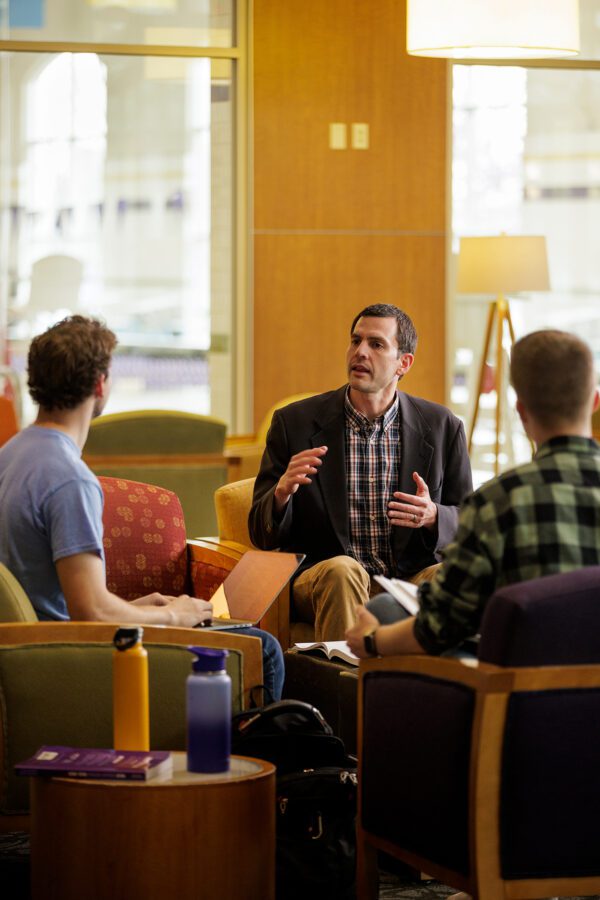 Professor sitting down having a conversation with two students