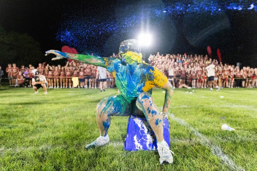 Male student pointing and smiling while covered in paint