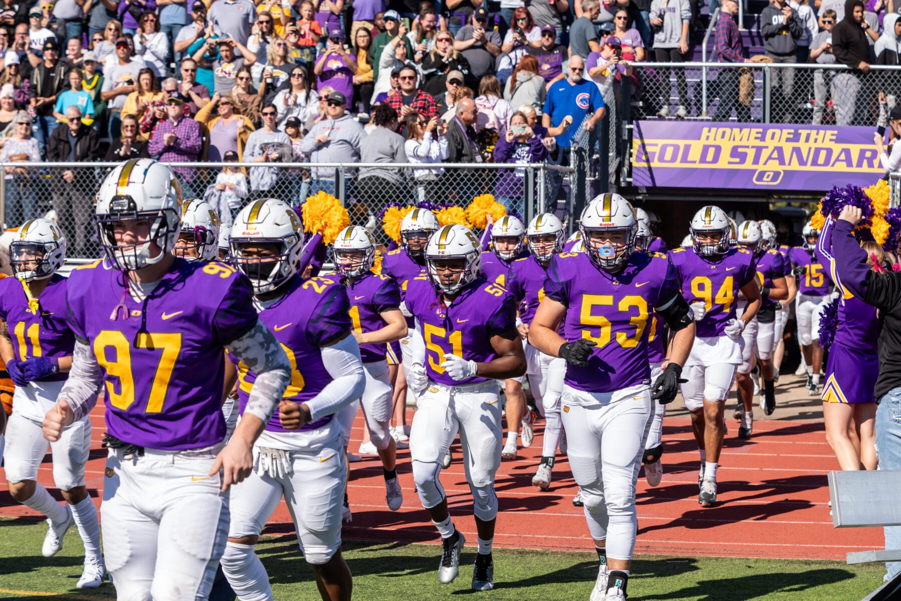 Olivet Football team runs out of the tunnel with audience cheering in background.