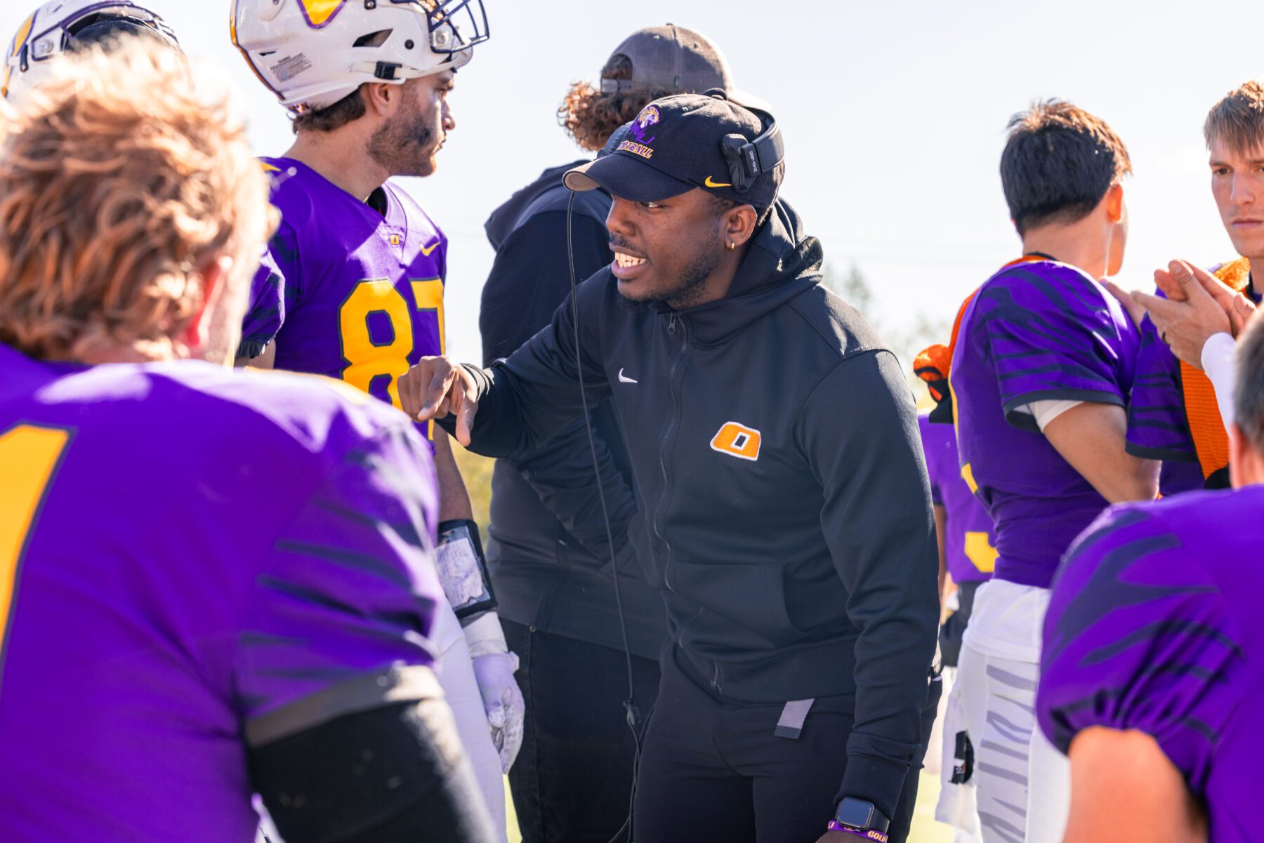 Olivet football coach talks to his players in a close huddle.