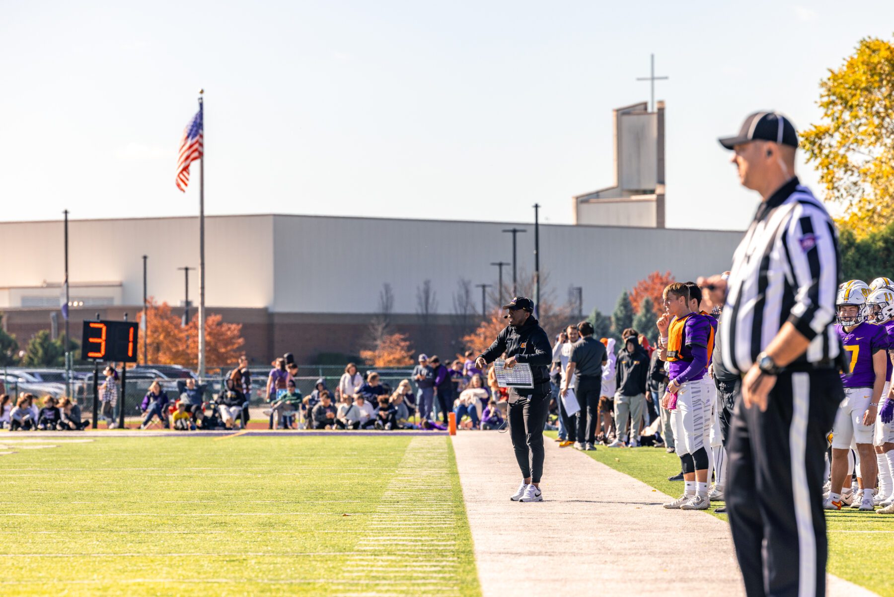 Olivet Football Coach walks the sideline talking to players on the field.
