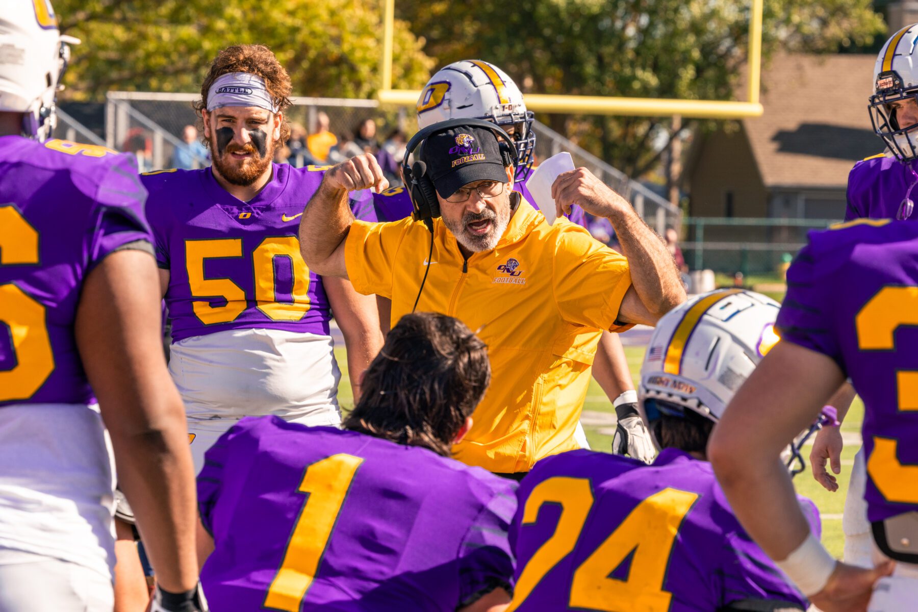 Olivet football coach talks to his players in a close huddle.