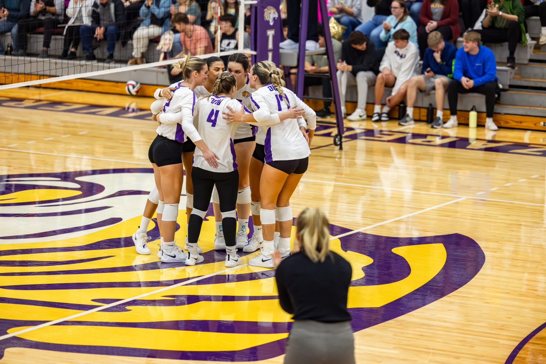 The women's volleyball team huddles up to celebrate after taking a point in the match.