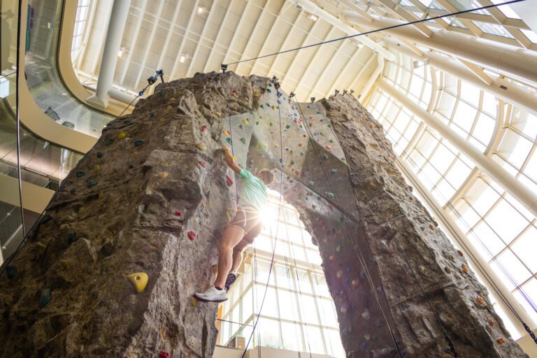male student climbing rock wall
