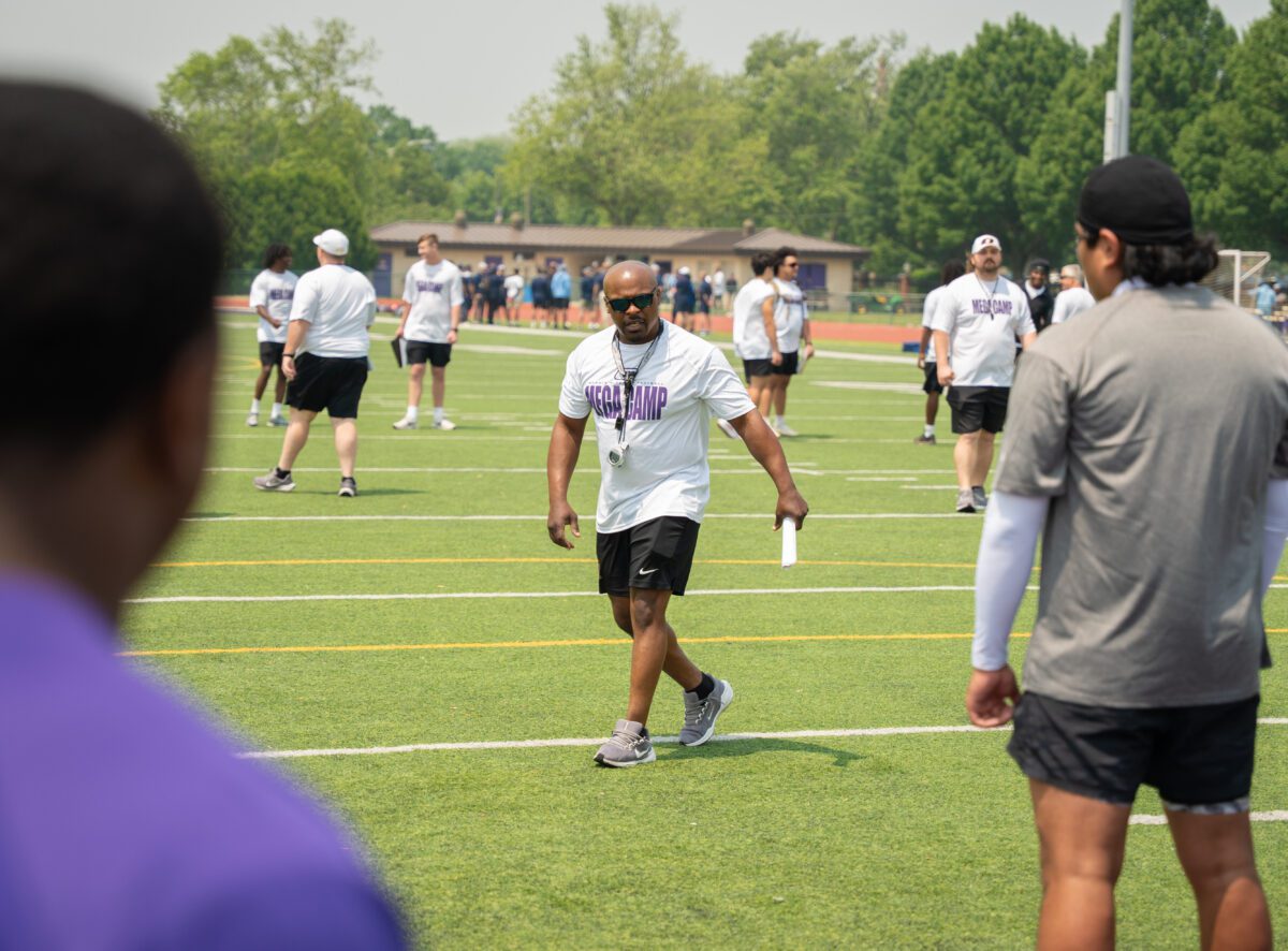 Coach walks across the field with whistle and clipboard during the 2025 Avante Mitchell Football Mega Camp at Olivet Nazarene University