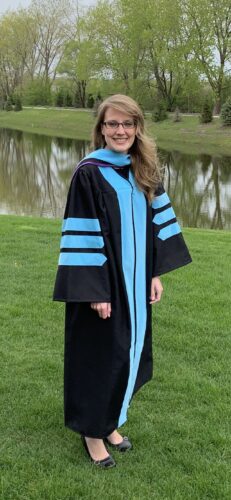 Katie standing in graduation regalia standing in front of a pond.
