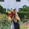 Jeanie holding flowers in a garden with a white house in the background.