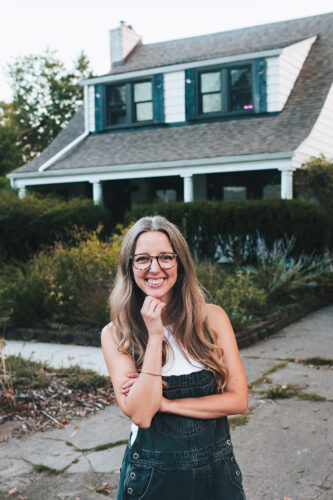 Janie standing in front of a White House with green shutters.