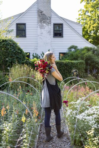 Janie standing in a garden with a White house in the background.