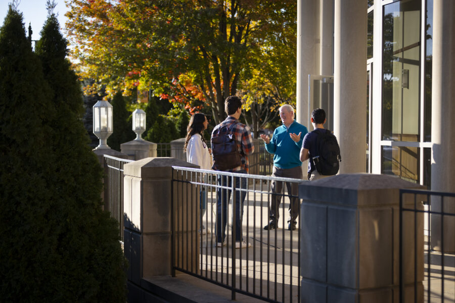 Professor talking to three students right outside a building