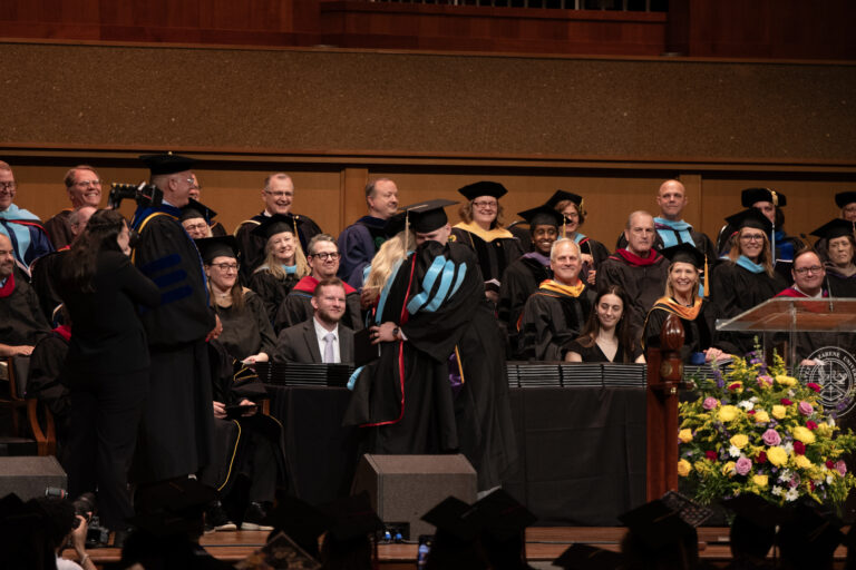Picture of a graduate and professor on stage.