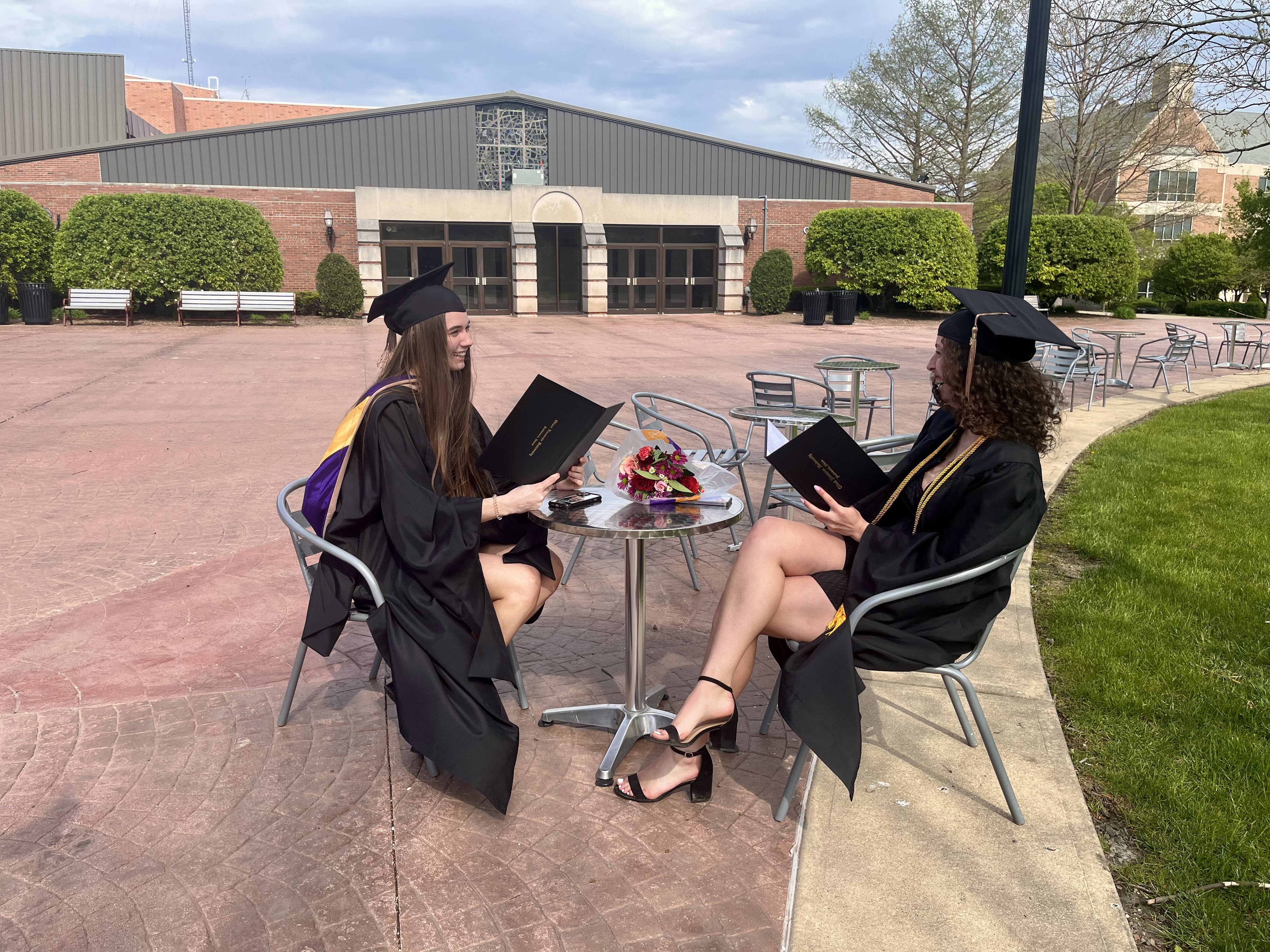 Mia with her sister in their graduation regalia sitting at a table.